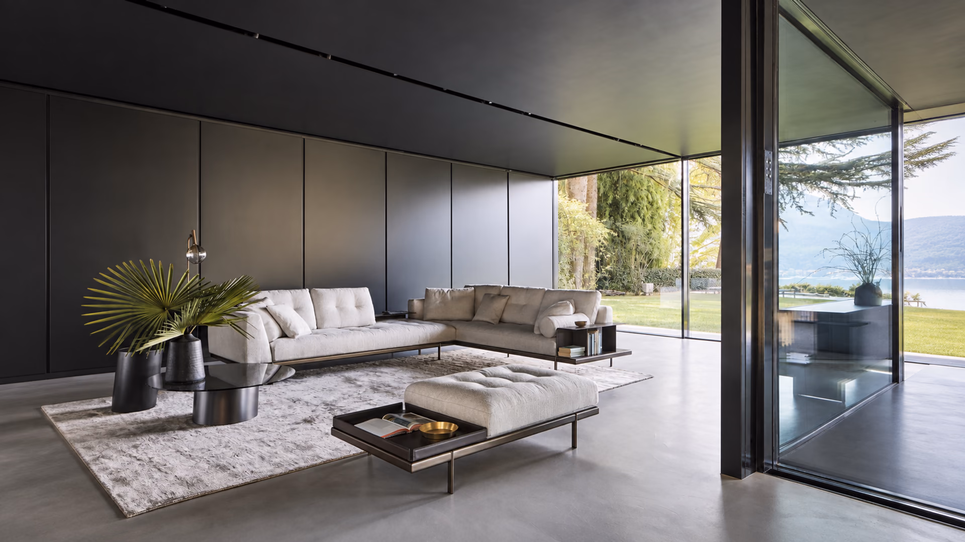 Bonaldo pale sectional sofa and upholstered ottoman with slim dark frames in a modern glass-walled living room.