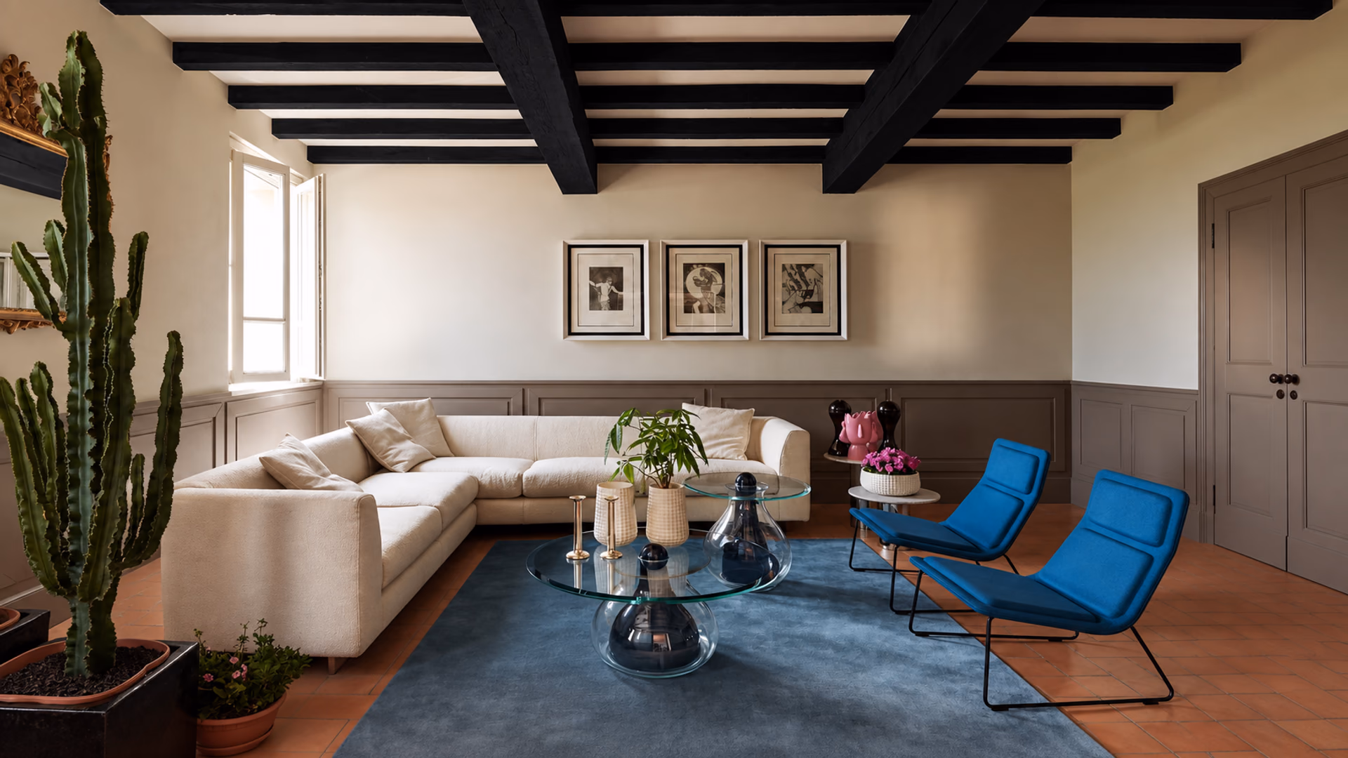 Cappellini pale corner sofa and blue lounge chairs with glass tables beneath dark ceiling beams.