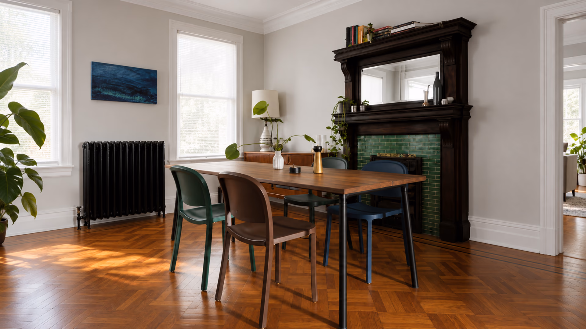 Emeco dining chairs in muted colors around a wood table beside a tiled fireplace.