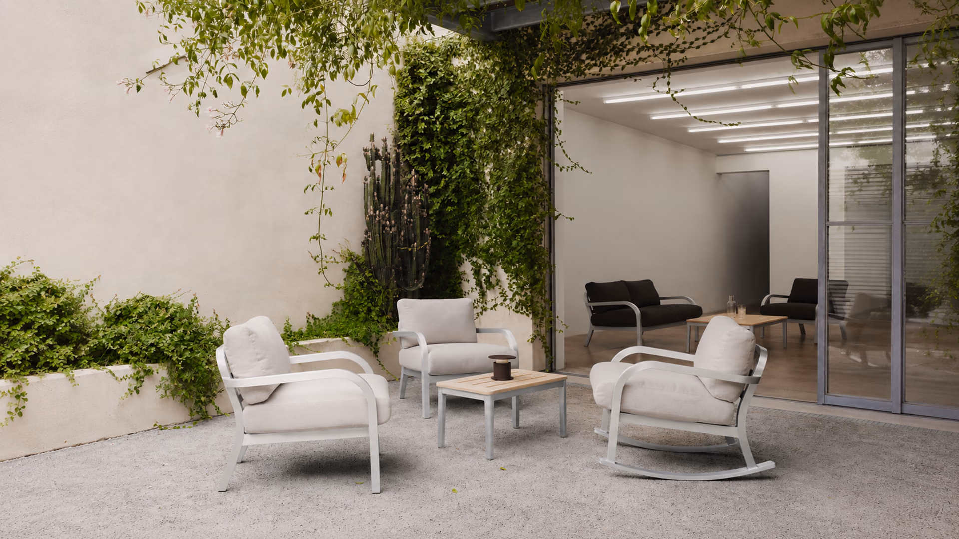 Emeco aluminum lounge chairs and a rocking chair with pale cushions on a planted courtyard terrace.