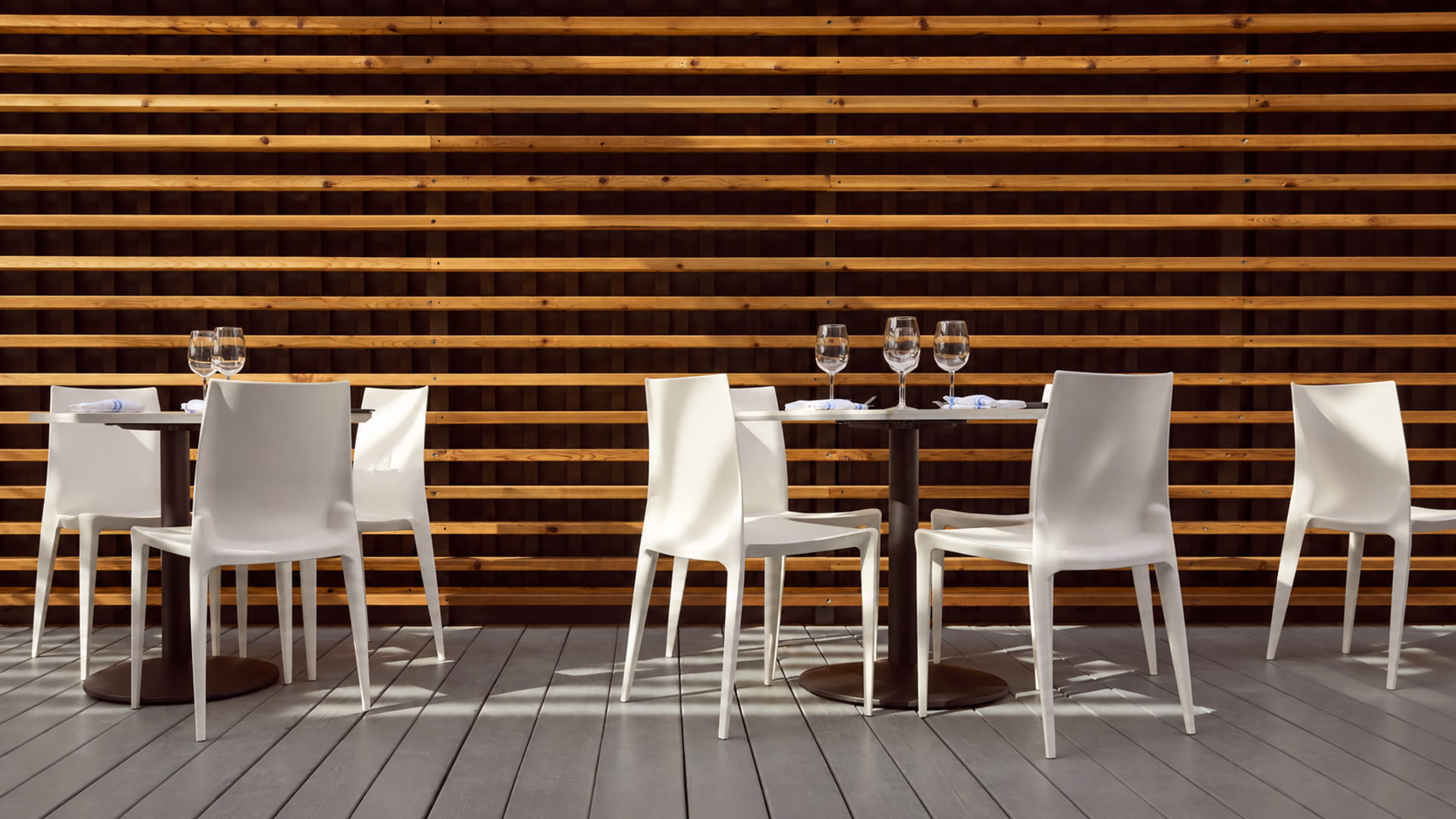 White Heller Bellini chairs at outdoor dining tables against a timber screen
