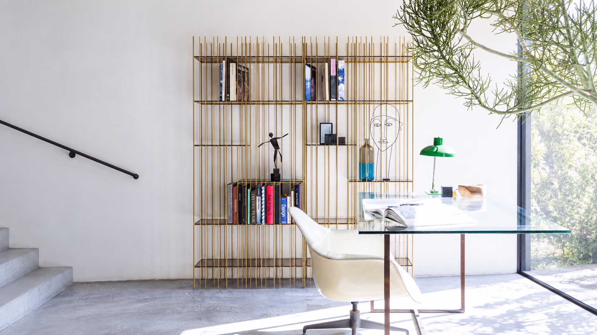 Mogg Metrica brass-toned bookcase beside a glass desk and white chair