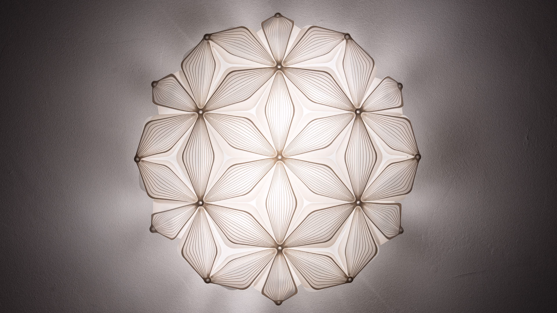 A glowing white Slamp C'est La Vie ceiling lamp with layered petal shapes on a dark wall