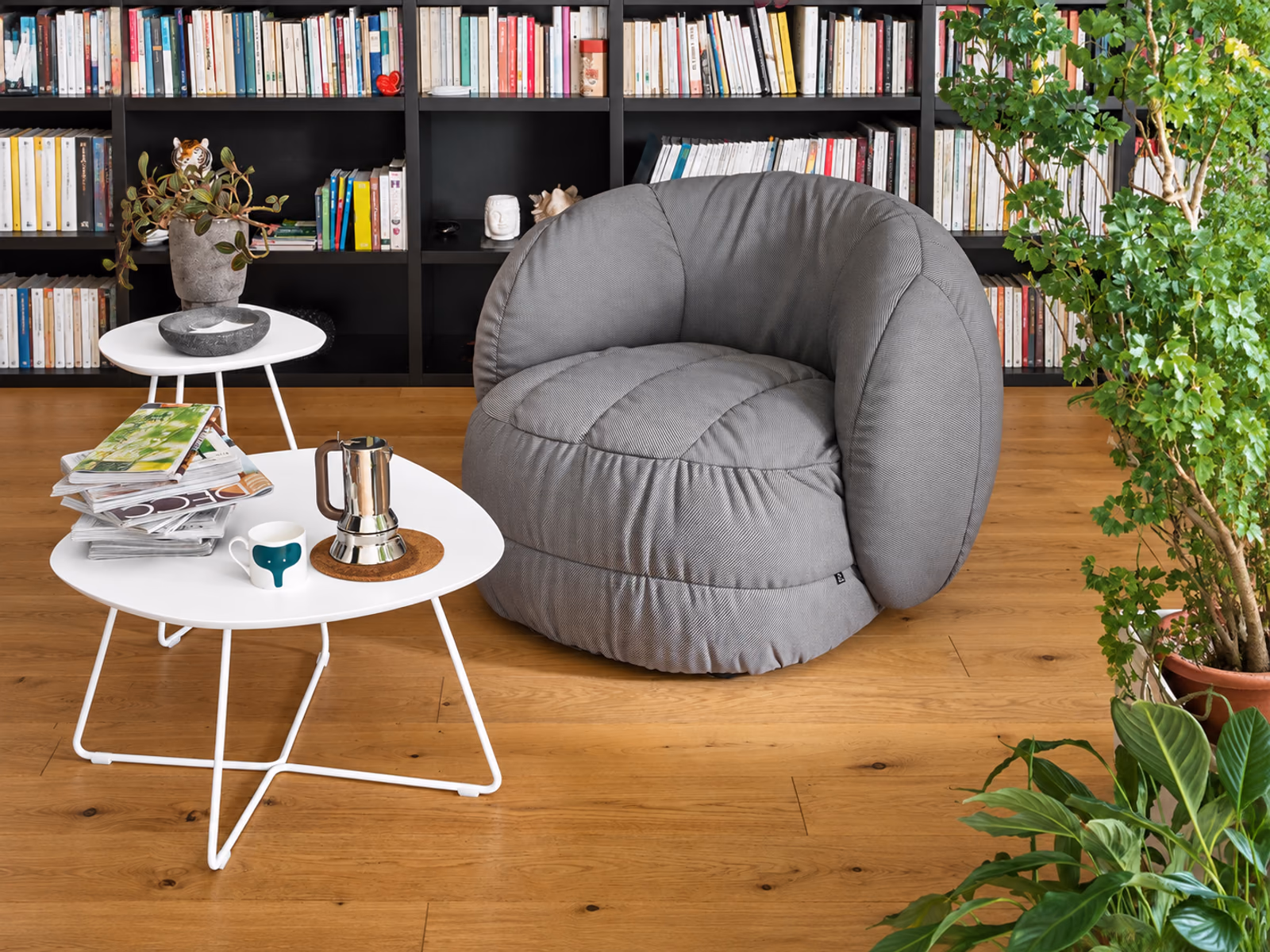 Connubia: A gray Ciop armchair creates a reading spot beside white occasional tables and a wall of books.