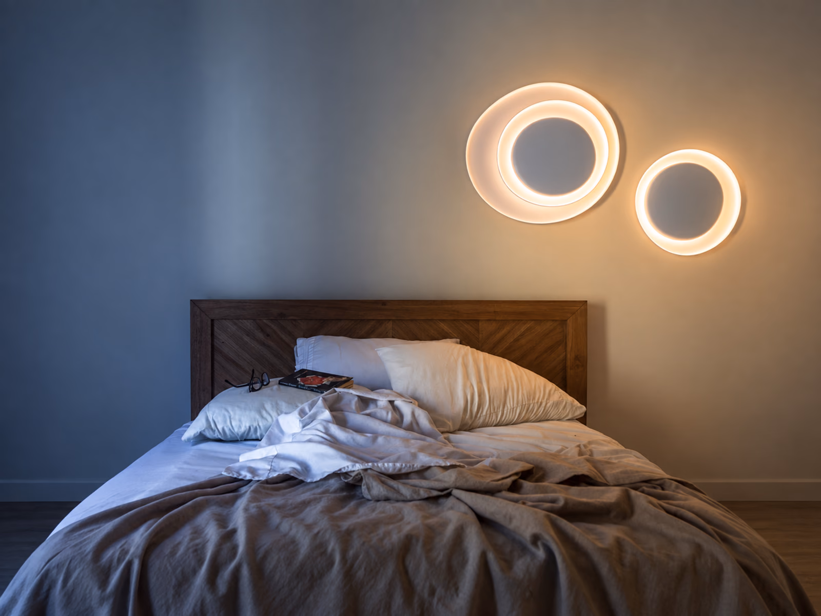 Foscarini: Glowing circular wall lights provide sculptural accents above an upholstered bed.