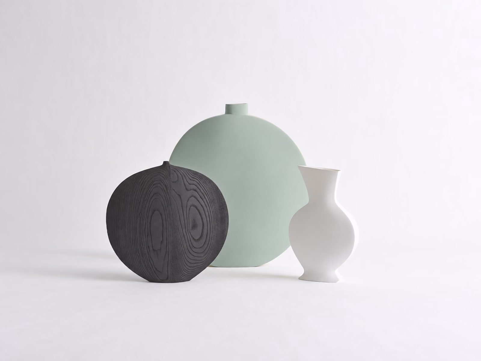 Kose: A dark wood-grain vessel is paired with pale green and white sculptural vases.