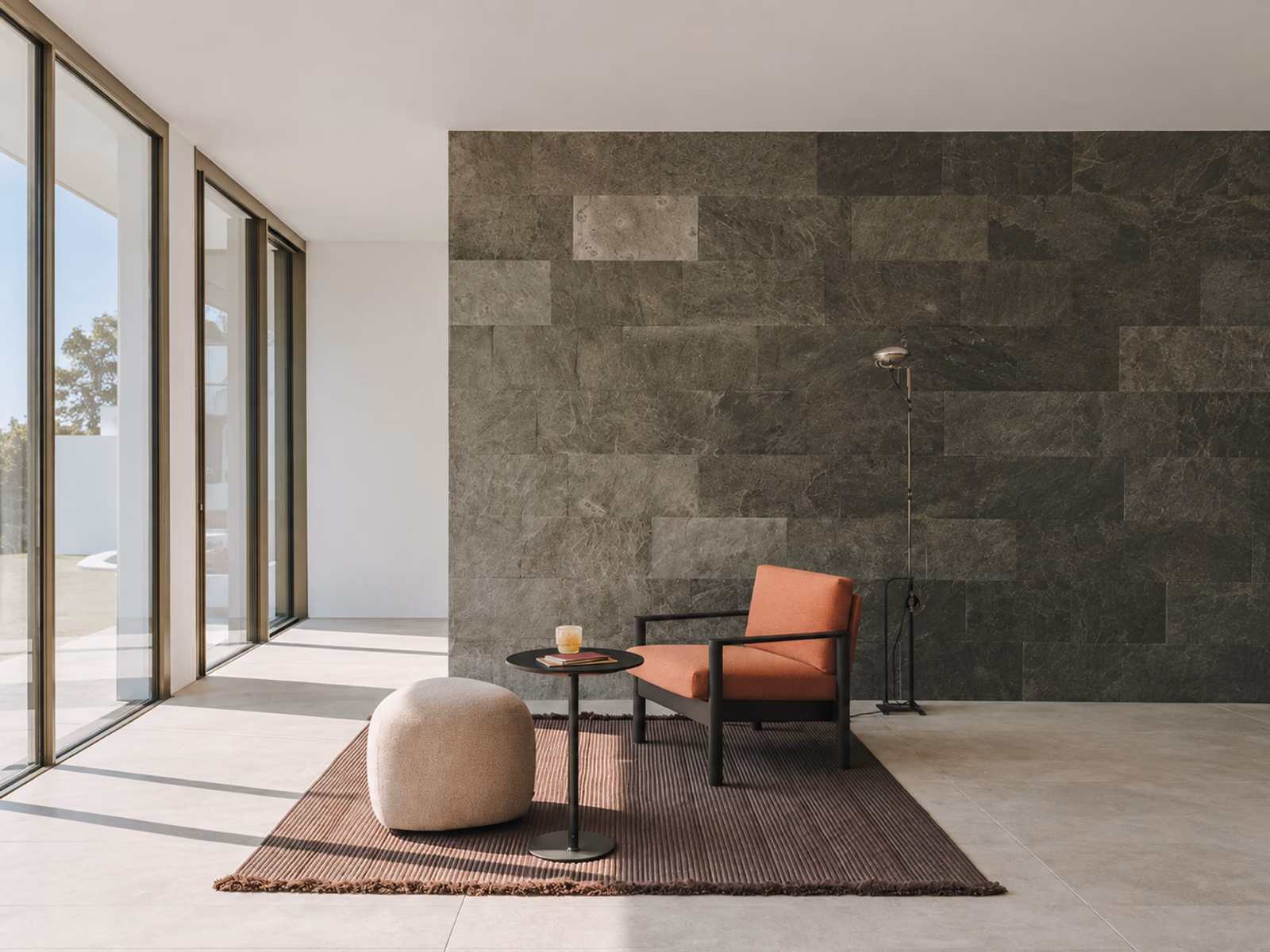 LaPalma: An orange lounge chair and a pale footrest sit beside a green stone wall.
