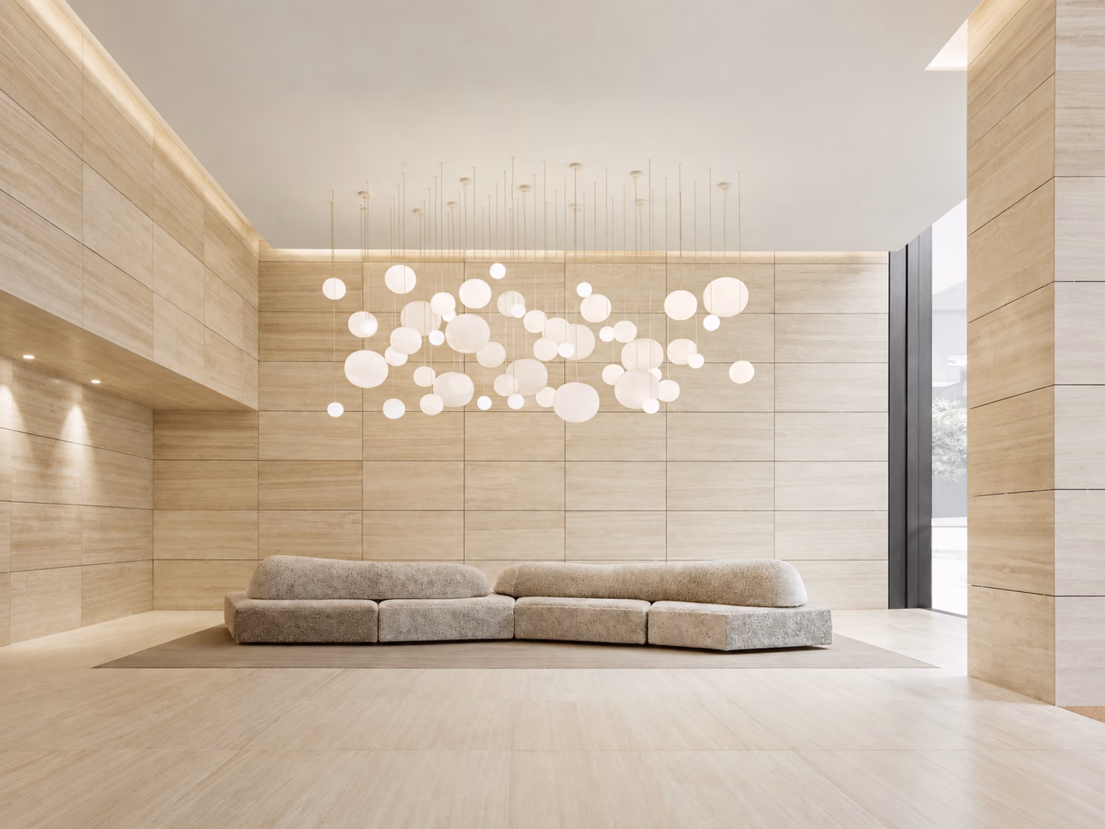 Lodes: A cluster of glowing Volum pendants hangs above a long upholstered sofa in a stone-lined room.