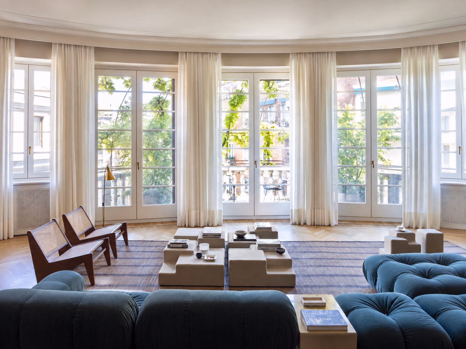 Mogg: Matrix tables sit between blue tufted sofas and wood lounge chairs in a curved, window-lined room.